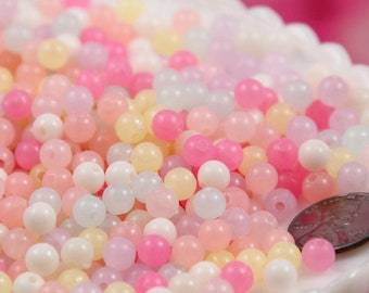 May include: A bowl filled with pastel-colored round beads. The beads are translucent and have a slight shimmer. The beads are in a variety of colors, including pink, yellow, blue, and white.