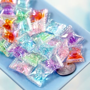 May include: A pile of iridescent, rainbow-colored, plastic, pillow-shaped charms. The charms are on a light blue surface.