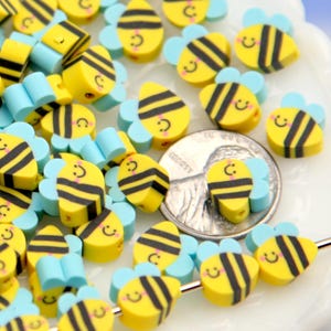 May include: A collection of yellow and black bee-shaped beads with light blue wings. Each bead has a smiling face. These decorative beads are ideal for crafting projects and jewelry making.
