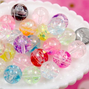 May include: A collection of colorful, transparent plastic beads. Each bead is spherical with a clear outer shell and contains iridescent glitter and colorful accents. The beads are in various colors, including pink, purple, yellow, and red.