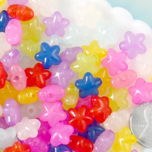 May include: A collection of colorful plastic star and oval shaped beads. The beads are translucent and have a glossy finish. A US penny is included for scale.