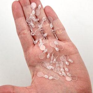 May include: A pile of clear plastic earring backs with a small loop on the back.