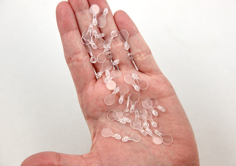 May include: A pile of clear plastic earring backs with a small loop on the back.