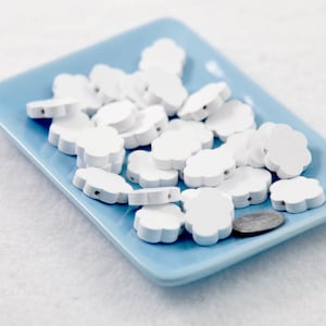 Könnte beinhalten: Ein blauer Teller gefüllt mit weißen, blumenförmigen Holzperlen. Die Perlen haben ein Loch in der Mitte zum Auf fädeln.