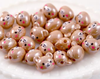 May include: A collection of brown bear-shaped beads with black eyes, small ears, and pink cheeks. The beads have a glossy finish and a hole for stringing. These decorative beads are ideal for jewelry making and crafting projects.