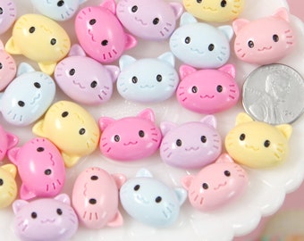 May include: A selection of pastel-coloured cat-shaped embellishments. The cat faces are in shades of pink, yellow, and blue, each with black eyes and a smiling mouth. These small, decorative pieces are ideal for crafting and adding a cute touch to various projects.
