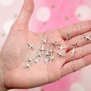 Puede incluir: Una colecci&oacute;n de abalorios de estrella plateados con anillas de salto. Los abalorios est&aacute;n esparcidos en una mano.
