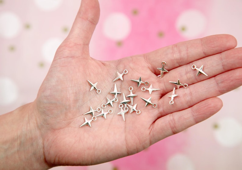 Puede incluir: Una colecci&oacute;n de abalorios de estrella plateados con anillas de salto. Los abalorios est&aacute;n esparcidos en una mano.