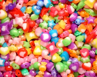 Può includere: Primo piano di un assortimento di perline colorate di varie forme. Le perline includono stelle, cuori e fiori in tonalità di rosso, rosa, blu, verde, giallo, arancione e viola. Ideale per la creazione di gioielli e l'artigianato.
