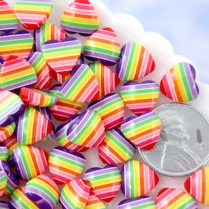 以下が含まれることがあります： 虹色のストライプが入った、カラフルなハート型の装飾品のコレクション。ハートは様々なサイズで、白いスカラップエッジの皿に並べられています。サイズの参考として、米国のペニーが含まれています。