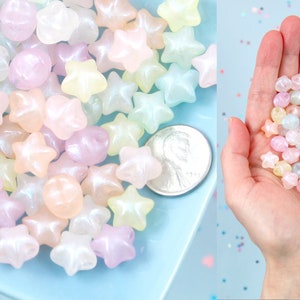 May include: A close-up of a pile of pastel-colored star-shaped beads. The beads are translucent and have a shimmery finish. A US quarter is included for scale.