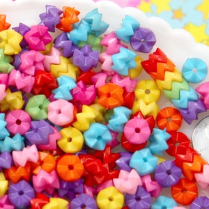 Può includere: Una collezione di perline di plastica colorate in varie forme, tra cui stelle, fiori e disegni geometrici. Le perline sono nelle tonalità di rosso, arancione, giallo, verde, blu e viola. Le perline sono in un piatto bianco smerlato.