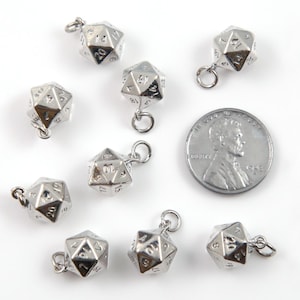 May include: Silver-colored, multi-sided dice charms with numbers, perfect for jewelry making or gaming. The charms are shown with a penny for size comparison. The dice have a small loop for attaching to a chain or other jewelry.