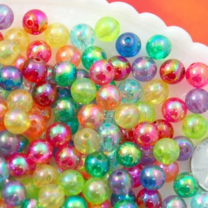 May include: A large assortment of iridescent plastic beads in various colors, including green, blue, pink, yellow, and orange. The beads are round and have a glossy finish.