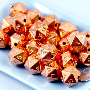 May include: A group of 18 copper-colored dice with numbers 1 through 12 on each face. The dice are arranged in a pile on a light blue surface.