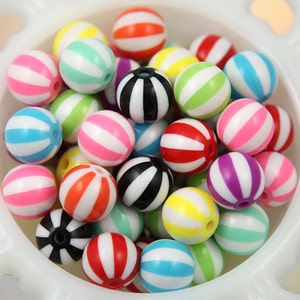 Può includere: Una collezione di perline colorate a righe in varie tonalità, tra cui rosa, blu, verde, giallo, arancione, rosso e nero. Le perline sono rotonde e hanno un foro per l'infilatura. Sono esposte in una ciotola bianca decorativa. Adatte per la creazione di gioielli e artigianato.