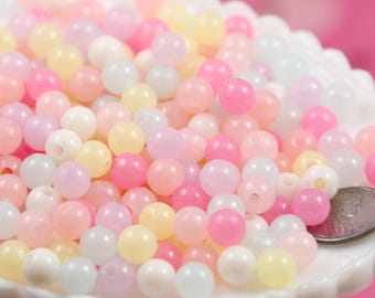 May include: A close-up of a pile of pastel-colored plastic beads. The beads are round and have a smooth, glossy finish. They are perfect for making jewelry, crafts, and other projects.