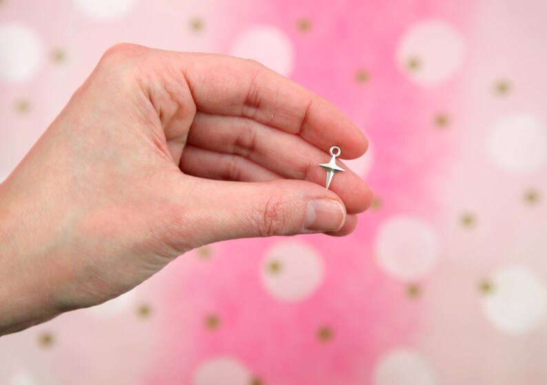 Puede incluir: Un charm de bailarina plateado con una falda en forma de estrella y un bucle en la parte superior.