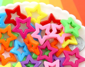 May include: A collection of colorful star-shaped beads in various shades including red, yellow, pink, orange, blue, green, and purple. The beads are scattered on a white, scalloped-edge dish, with a coin visible. The background features a rainbow gradient.