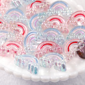 Pode incluir: Uma coleção de enfeites de plástico em forma de arco-íris iridescentes. Os enfeites têm um acabamento perolado.