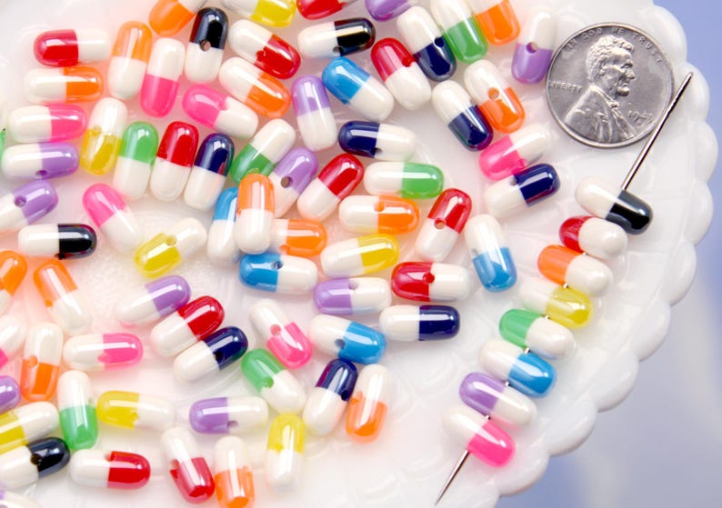 Puede incluir: Una colecci&oacute;n de cuentas coloridas en forma de c&aacute;psula en varios colores, incluyendo rojo, naranja, amarillo, verde, azul, morado y negro. Una moneda y una aguja sugieren un tema de artesan&iacute;a o joyer&iacute;a.