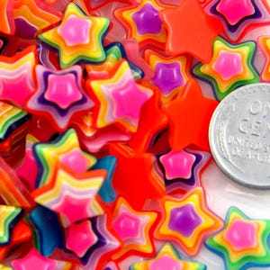 May include: A close-up of a pile of colourful rainbow star-shaped buttons. The buttons are layered and have a glossy finish. A US penny is in the background.
