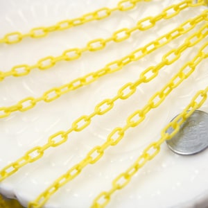 May include: A close-up of a yellow plastic chain. The chain is lying on a white surface.