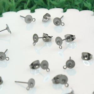 May include: A collection of stainless steel earring posts and backs. The posts have a flat disc with a loop for attaching charms, and a straight post. The earring backs are butterfly style.