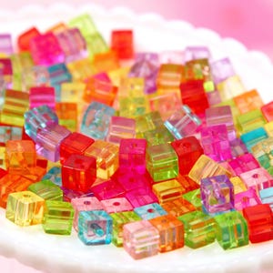 May include: A collection of colorful, transparent, square-shaped beads. The beads are made of acrylic and are perfect for jewelry making or crafting.