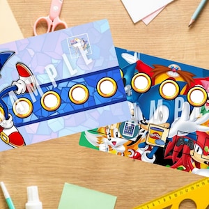 Può includere: Due carte da gioco stampabili con personaggi della serie di videogiochi Sonic the Hedgehog. La prima carta presenta Sonic the Hedgehog in uno schema di colori blu e bianco con anelli dorati. La seconda carta presenta Sonic, Tails, Knuckles, Amy Rose e il Dr. Eggman in uno schema di colori blu, rosso, giallo e rosa con anelli dorati.