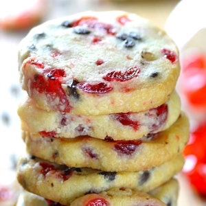 May include: A stack of shortbread cookies with chocolate chips and dried cranberries. The cookies are light brown and have a slightly golden hue. The cranberries are a vibrant red and the chocolate chips are dark brown.