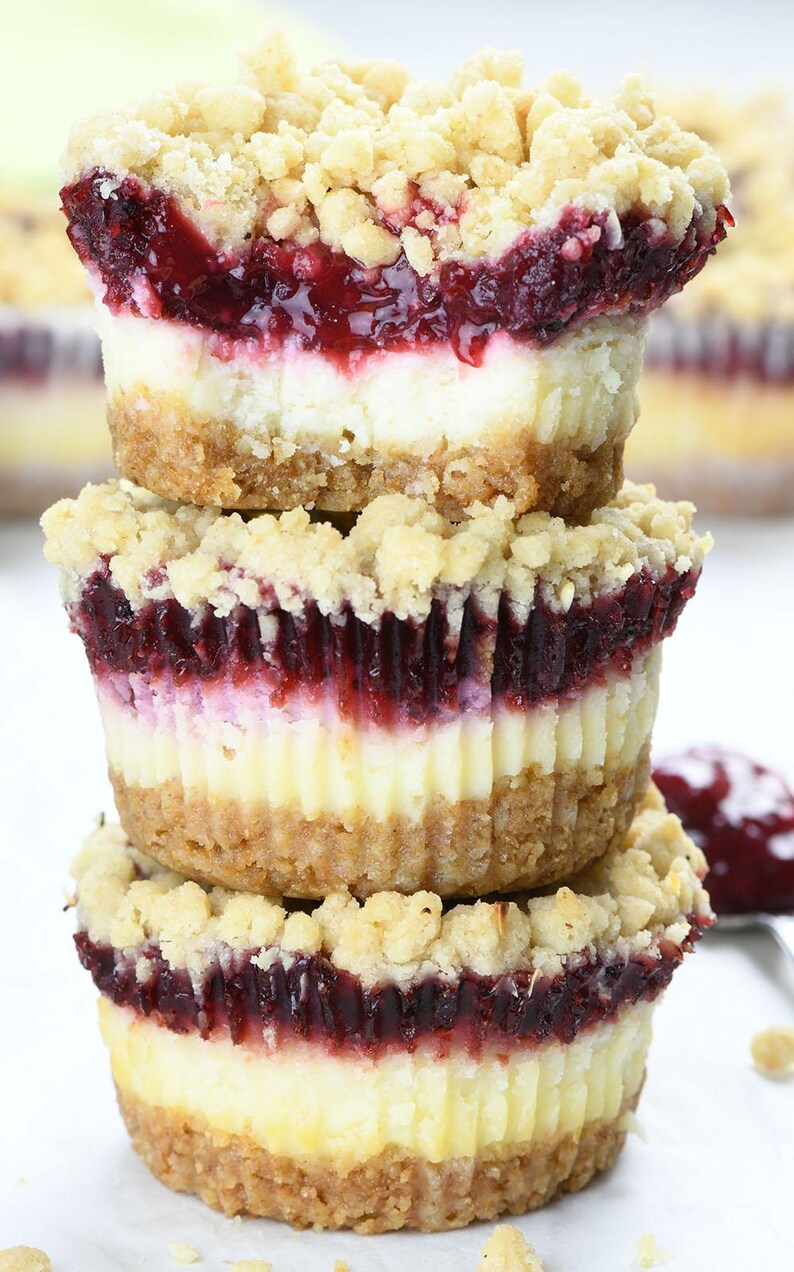 A stack of three cranberry mini cheesecakes highlighting their layers: crunchy graham cracker crust, creamy cheesecake, bright cranberry filling, and crumbly streusel topping, creating a festive dessert display.