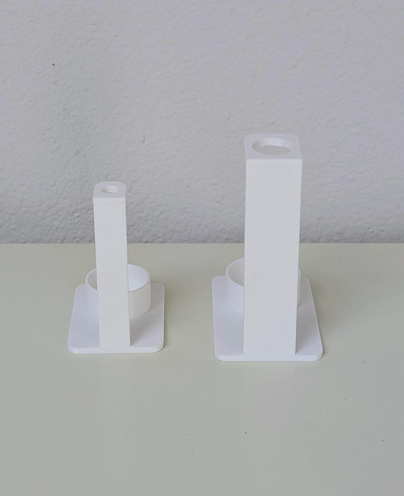 May include: Two white plastic toothbrush holders, each with a small round opening at the top and a larger round opening at the bottom. The holders are of different sizes.