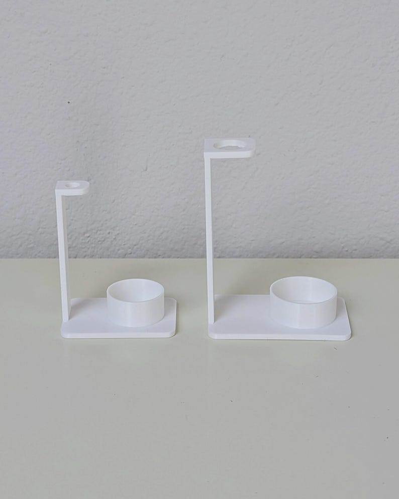 May include: Two white plastic toothbrush holders with a small cup for toothpaste. The holders are different sizes.