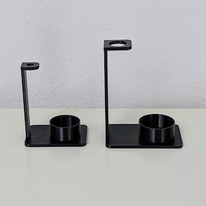 May include: Two black plastic toothbrush holders with a round base and a vertical stand with a circular opening at the top.