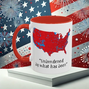 May include: White ceramic coffee mug with a red rim and handle. The mug features a map of the United States with red and blue counties. The text "Unburdened by what has been" is printed below the map.