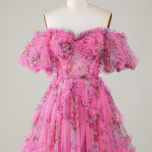 May include: A bright pink, off-the-shoulder dress with layers of ruffled tulle. The dress has a floral print and a fitted waist. The short sleeves and skirt are adorned with cascading ruffles, creating a voluminous silhouette.
