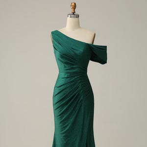 Könnte beinhalten: Ein schimmerndes, smaragdgrünes, bodenlanges Kleid mit einem Schulterträger und einem Schlitz an der Seite.