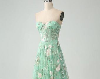 Puede incluir: Un vestido de tul verde menta sin tirantes, con un corpiño ajustado y una falda completa. El vestido está adornado con delicados bordados florales.