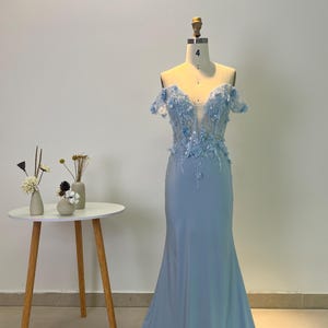Peut inclure: Une robe bleu ciel à épaules dénudées avec un corsage ajusté et une jupe fluide. Le corsage est orné de broderies florales délicates et de paillettes.