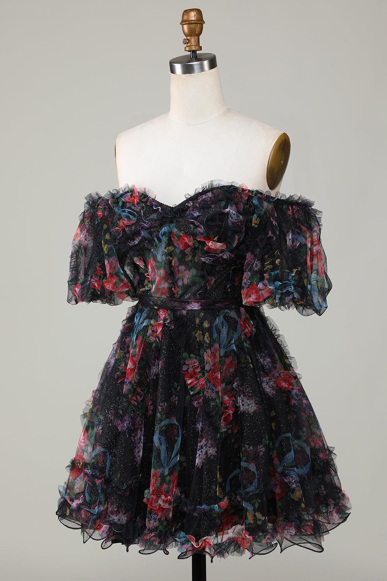 May include: A black off-the-shoulder dress with a floral pattern in red, blue, and purple. The dress has a ruffled neckline and sleeves, and a fitted waist. The skirt is flared and has ruffles.