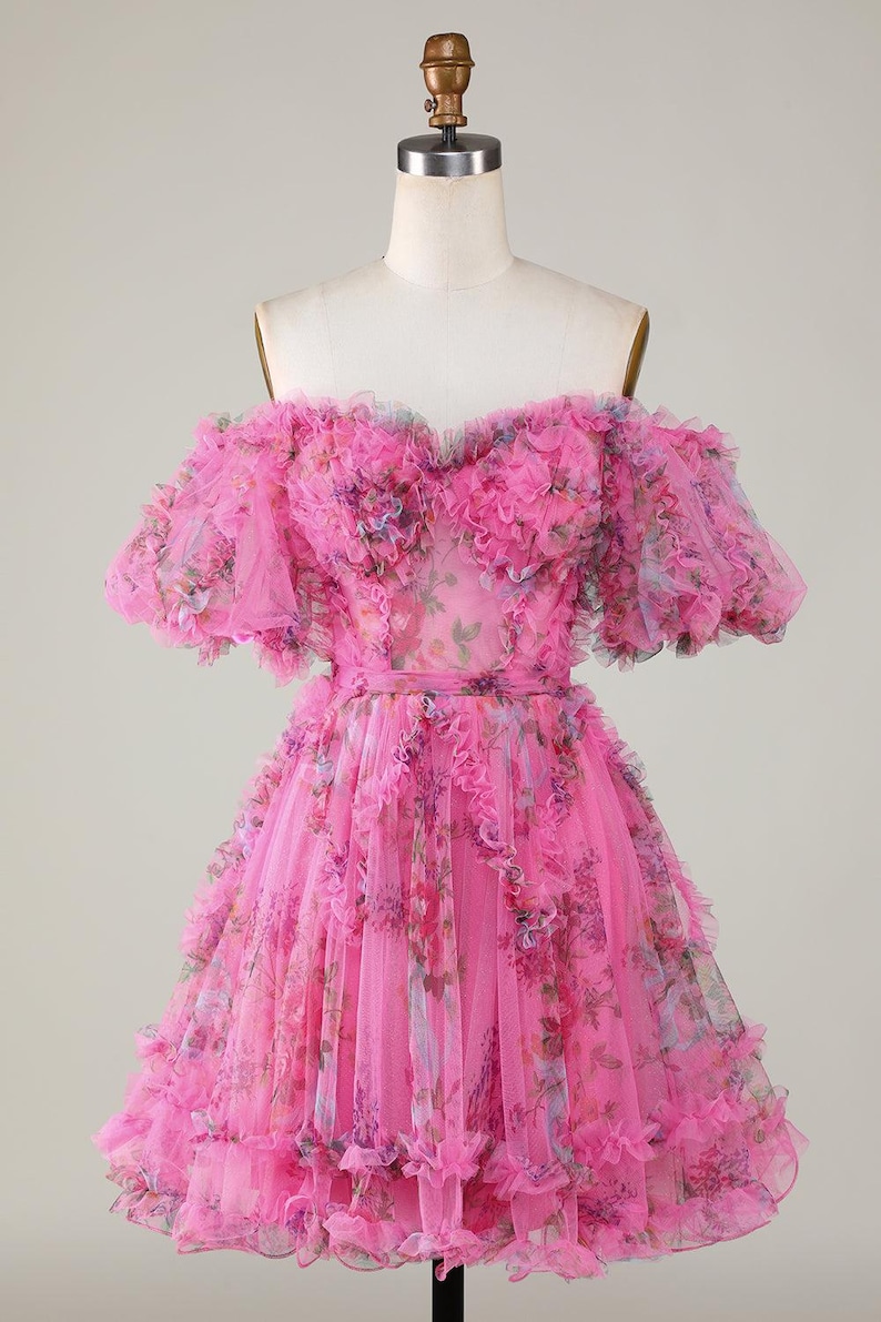 May include: A bright pink, off-the-shoulder dress with layers of ruffled tulle. The dress has a floral print and a fitted waist. The short sleeves and skirt are adorned with cascading ruffles, creating a voluminous silhouette.