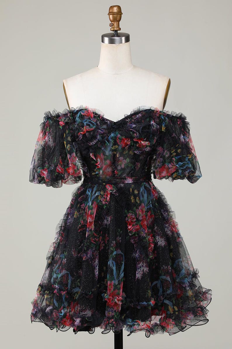 May include: Black off-the-shoulder dress with a floral pattern in red, blue, and purple. The dress has a ruffled neckline, sleeves, and hem. The dress is displayed on a mannequin.