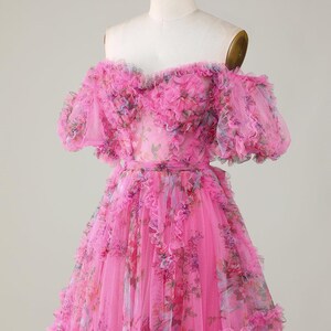 May include: A bright pink, off-the-shoulder dress with a floral design. The dress has layers of ruffled fabric and short sleeves. The bodice and skirt are decorated with a delicate floral print, creating a romantic and feminine appearance.