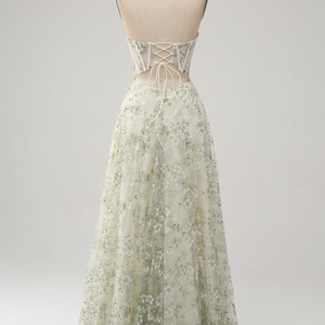 May include: A strapless, floor-length gown with a fitted bodice and a flowing skirt. The bodice is made of a sheer fabric with floral embroidery in shades of green and white. The skirt is made of a soft, flowing tulle fabric.