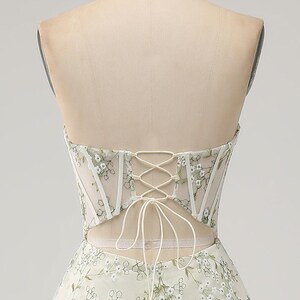 May include: A white strapless dress with a lace-up back and floral embroidery. The dress has a fitted bodice and a flowing skirt.
