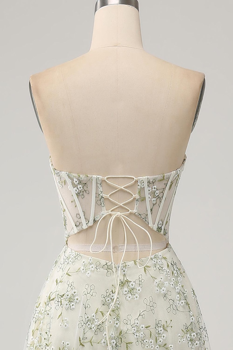 May include: A white strapless dress with a lace-up back and floral embroidery. The dress has a fitted bodice and a flowing skirt.