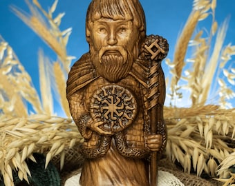 May include: A wooden carving of a bearded figure holding a shield with a sun symbol and a staff. The figure is wearing a tunic with intricate details. The carving is set against a background of wheat stalks.