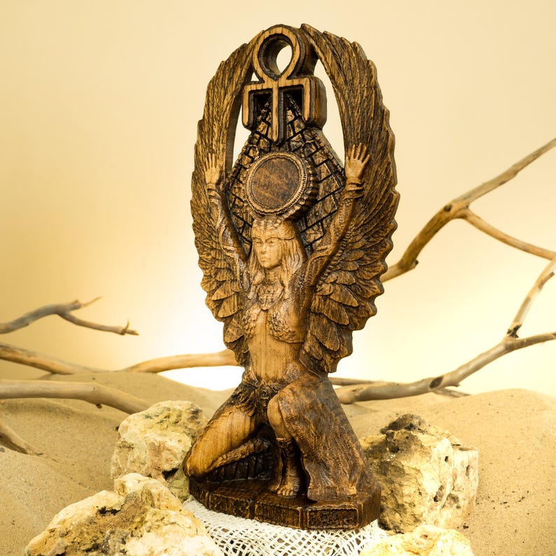 Może przedstawiać: Drewniana statua skrzydlatej bogini z symbolem ankh nad głową. Statua jest rzeźbiona z ciemnego brązu i ma szczeg&oacute;łowy wz&oacute;r.