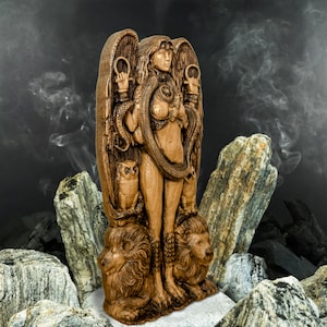 May include: A wooden statue of a female figure with wings, a snake, and owls. The figure is standing on two lions. The statue is brown and has a rustic finish.